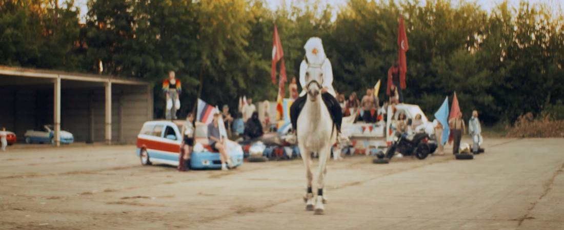 A rider on a white horse approaching a parade of decorated cars