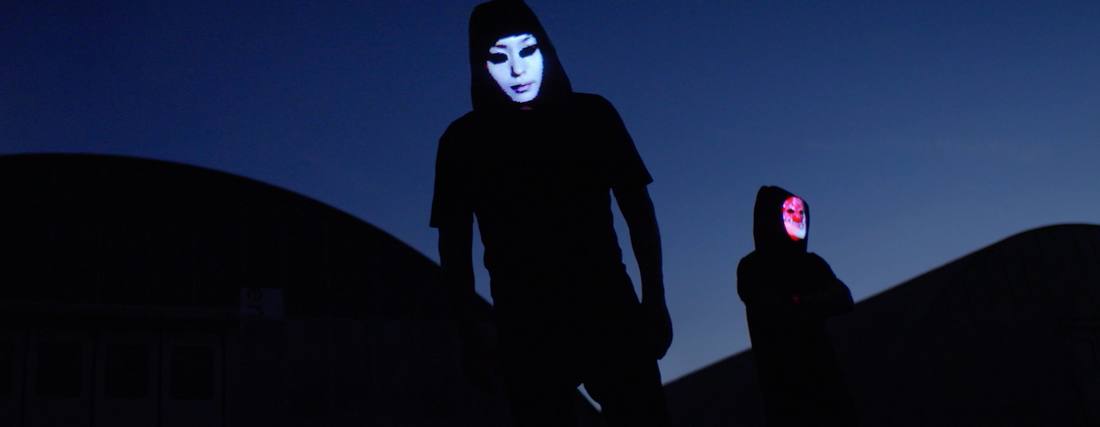Two figures with LED masks against the last blue of the sky